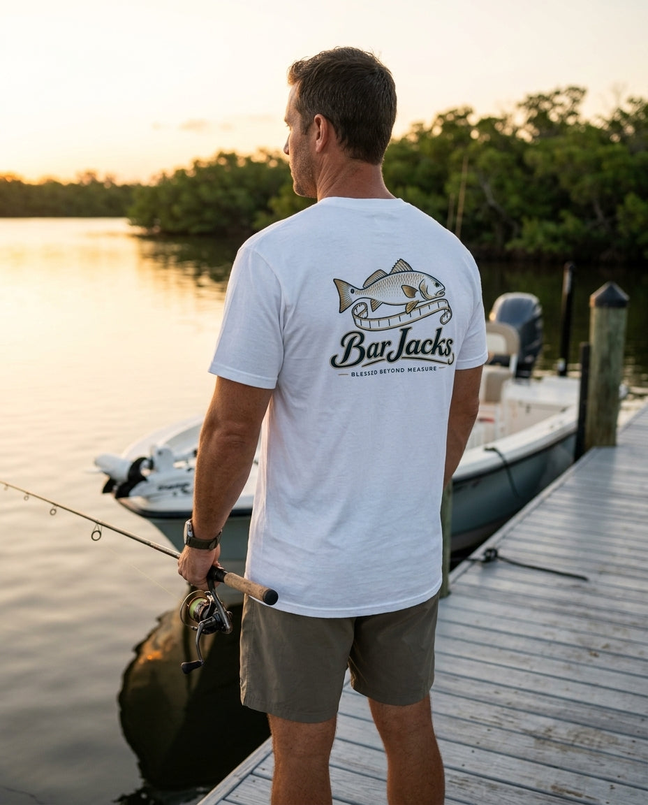 Man wearing the Bar Jacks Blessed Beyond Measure white men's cotton tee on a bay dock at sunrise, back print visible