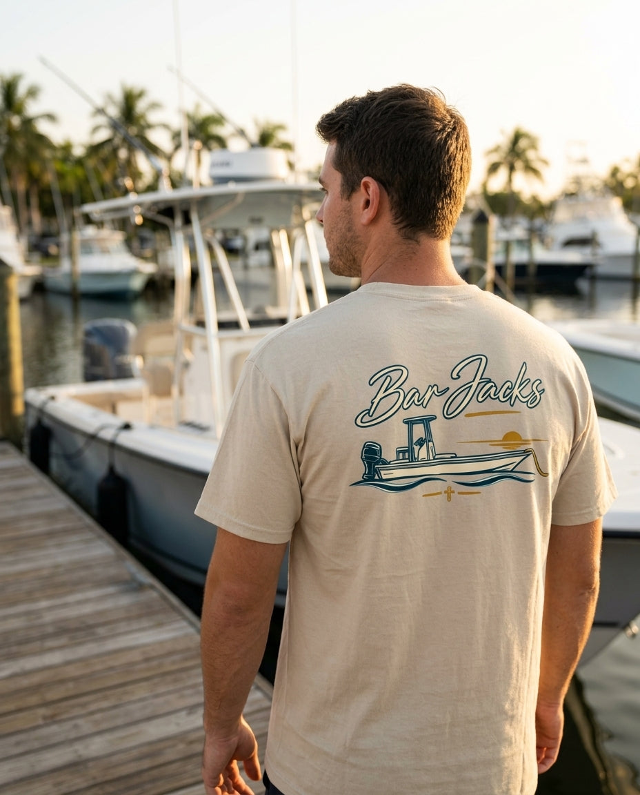 Man wearing the Bar Jacks Center Console Sunset tan cotton tee on a marina dock at golden hour, back print visible